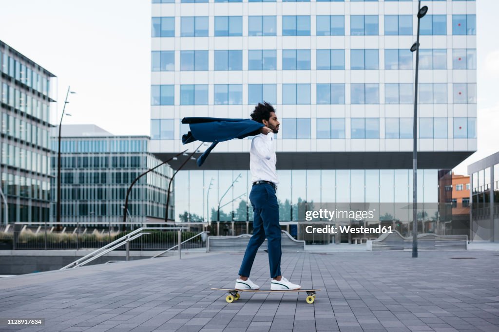 Spain, Barcelona, young businessman riding skateboard in the city