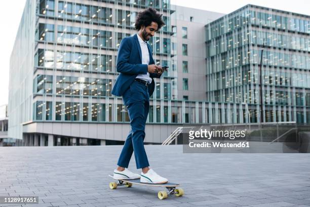 spain, barcelona, young businessman riding skateboard and using cell phone in the city - beruf sport stock-fotos und bilder