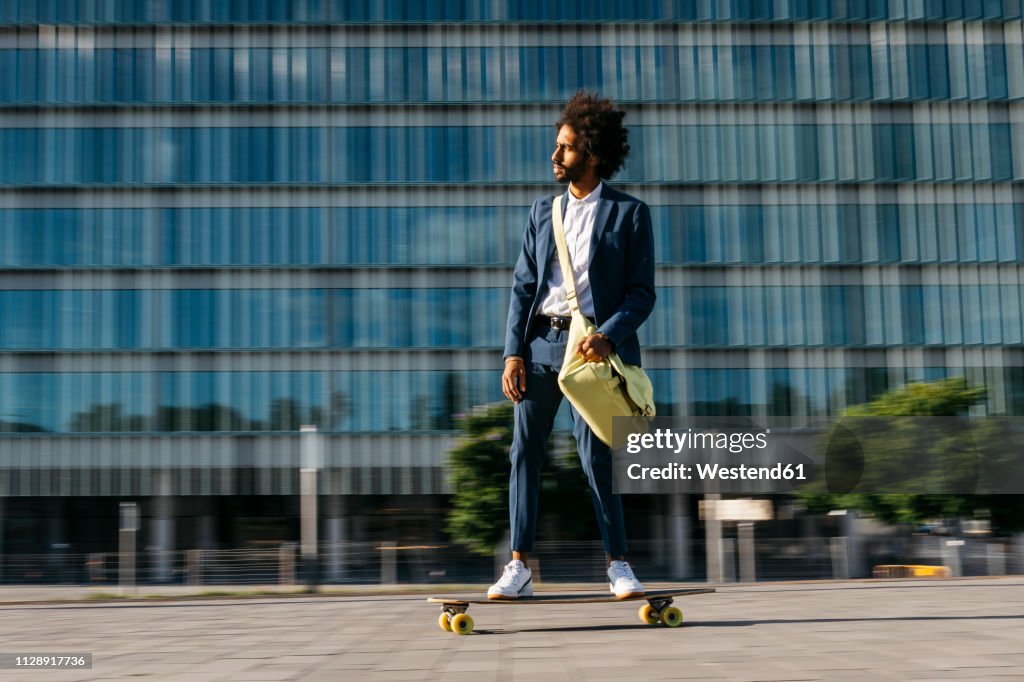 Spain, Barcelona, young businessman riding skateboard in the city