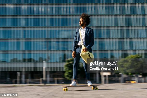 spain, barcelona, young businessman riding skateboard in the city - blue suit stock-fotos und bilder