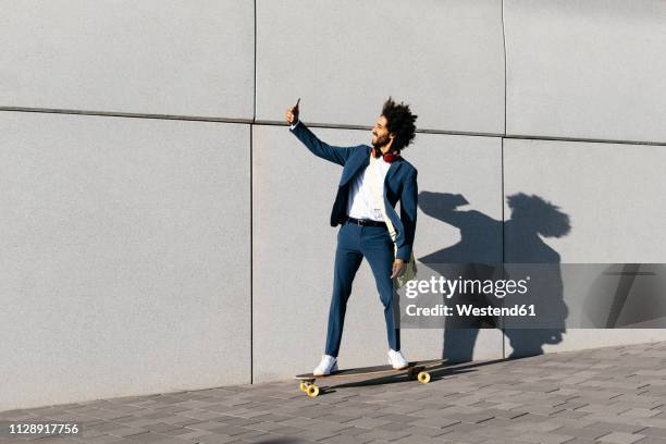 young businessman riding skateboard along a wall taking a selfie - man skateboard stock pictures, royalty-free photos & images