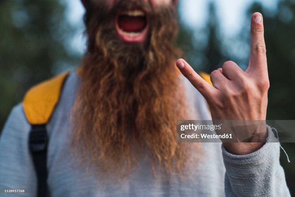 Close-up of screaming man with beard making horn sign