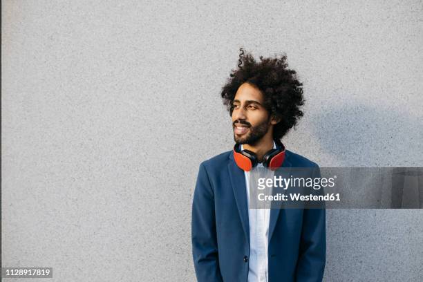smiling young businessman with headphones at a wall - sideways glance stock pictures, royalty-free photos & images