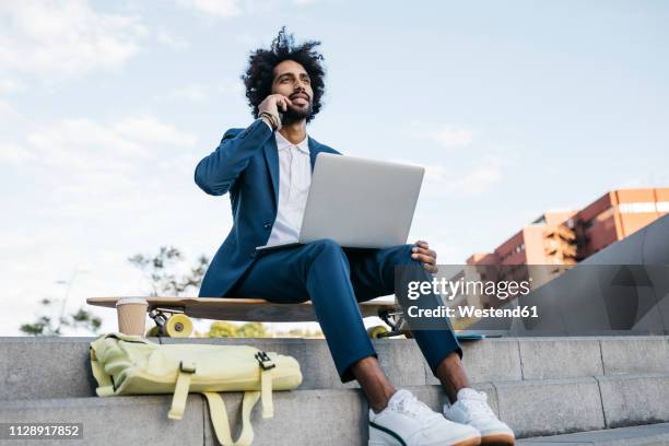 spain, barcelona, young businessman sitting outdoors in the city using cell phone and laptop - flexibility work stock pictures, royalty-free photos & images
