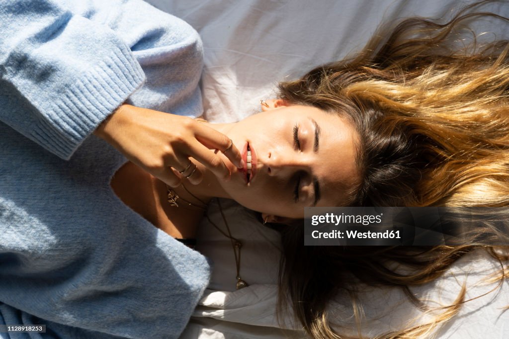 Portrait of beautiful young woman lying in bed with closed eyes