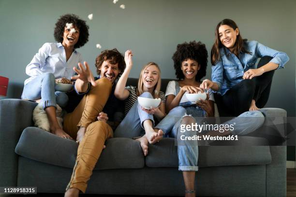 exuberant friends sitting on couch throwing popcorn - group on couch stock pictures, royalty-free photos & images