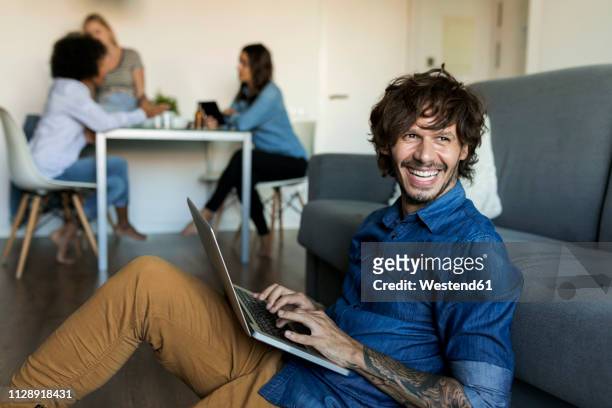 laughing man sitting on floor using laptop with friends in background - black woman happy white background foto e immagini stock