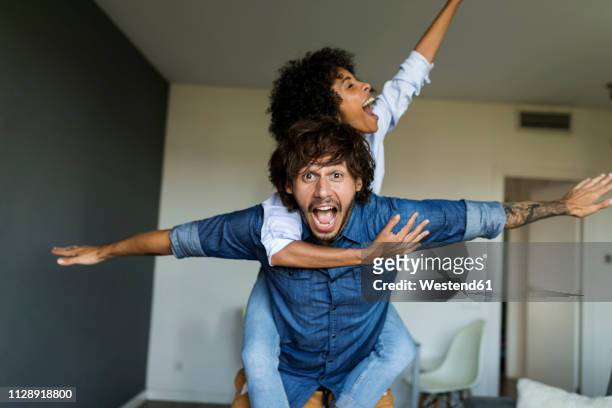 cheerful man carrying girlfriend piggyback at home - piggyback stock pictures, royalty-free photos & images
