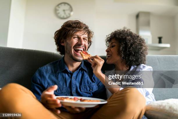 happy couple sitting on couch eating pizza - 30 39 años fotografías e imágenes de stock