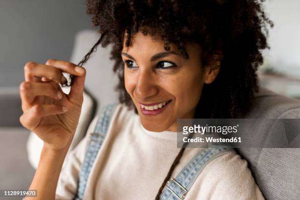 portrait of smiling woman sitting on couch at home examining her hair - examining hair stock pictures, royalty-free photos & images