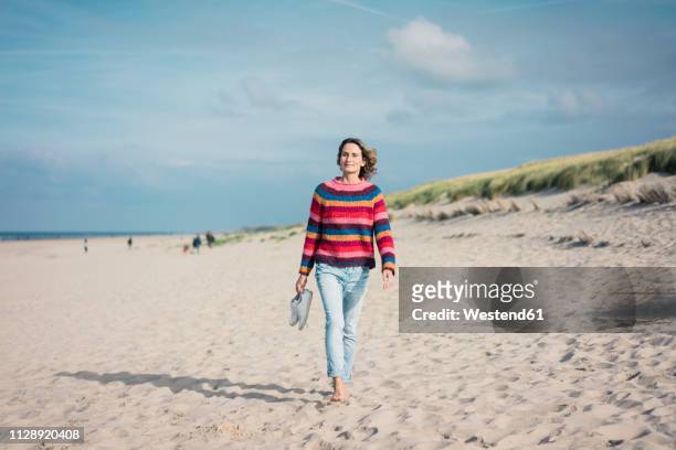 mature woman walking barefoot on the beach - netherlands women stock-fotos und bilder