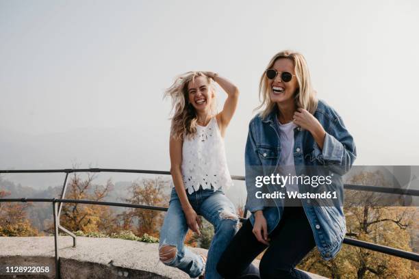 germany, black forest, sitzenkirch, two happy young women sitting on railing at sausenburg castle - german blonde 個照片及圖片檔