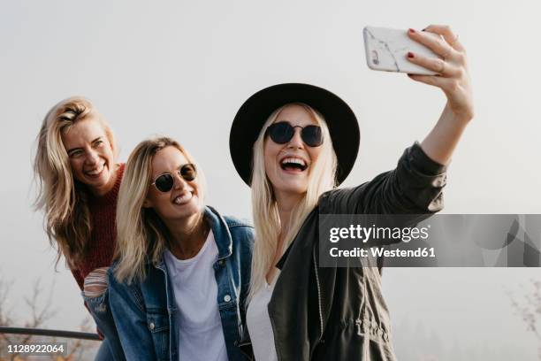 three happy young women taking a selfie outdoors - girlfriend stock-fotos und bilder
