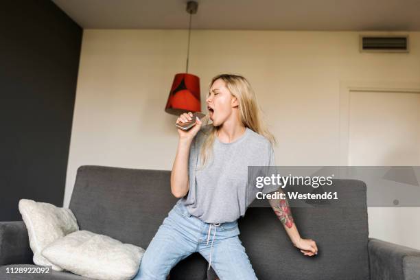 exuberant young woman on couch with cell phone pretending to sing - white trousers stockfoto's en -beelden