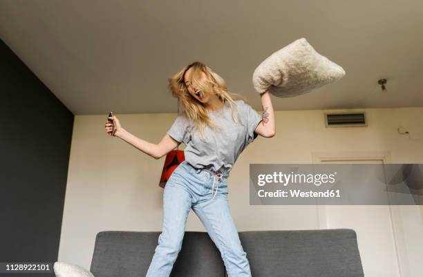 carefree young woman jumping on couch at home - hysteria fotografías e imágenes de stock