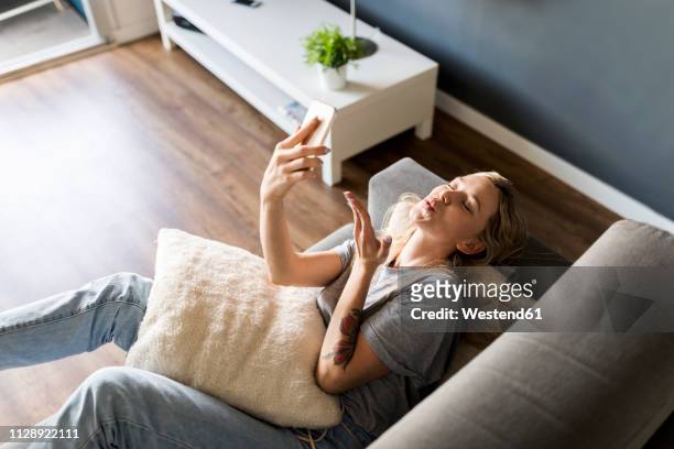 smiling young woman lying on couch taking a selfie - mandar um beijo imagens e fotografias de stock