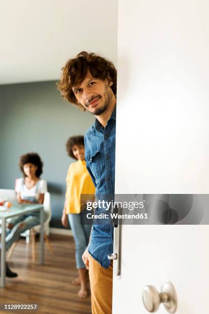 portrait of smiling man with friends in background opening the door - apartment door stock pictures, royalty-free photos & images