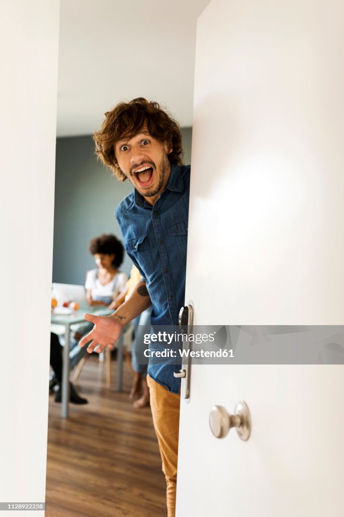 Portrait of surprised man with friends in background opening the door