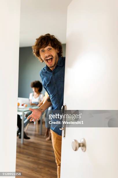 portrait of surprised man with friends in background opening the door - temptation stock pictures, royalty-free photos & images