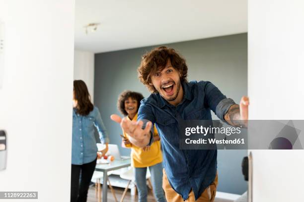 portrait of surprised man with friends in background opening the door - door opening stock-fotos und bilder