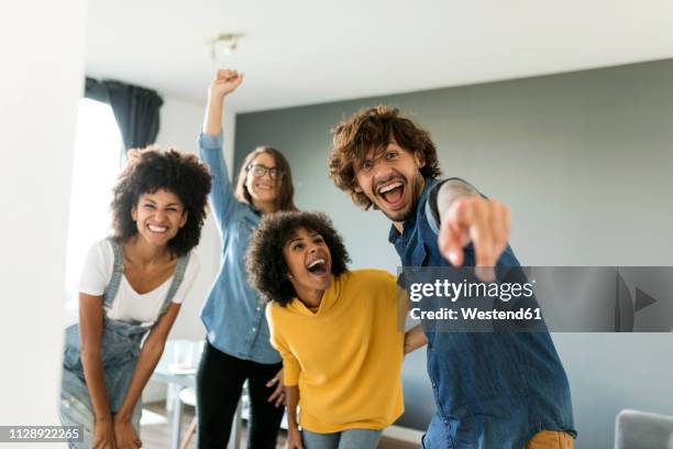 portrait of cheerful friends at home with man pointing his finger - happy millennial at home photos et images de collection