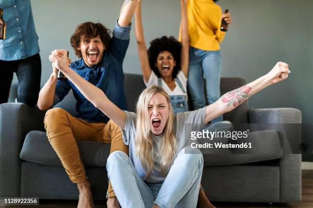 excited fans watching tv and cheering - happy millennial at home photos et images de collection