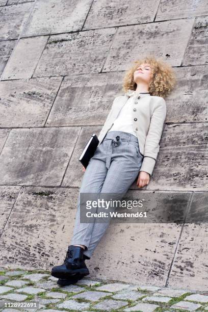 fashionable blond woman with folder leaning against wall having a rest - simple living stock pictures, royalty-free photos & images