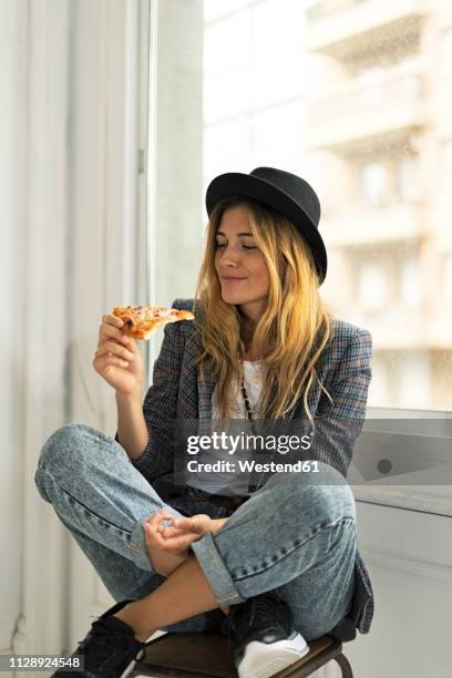 young woman in a studio eating pizza at the window - eating pizza stock pictures, royalty-free photos & images