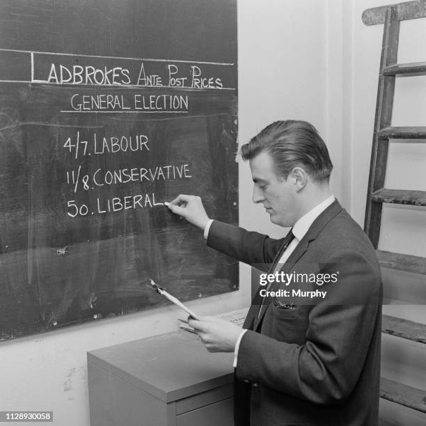 Man writes the general election forecasts on a blackboard at betting company Ladbrokes, UK, 18th October 1963.