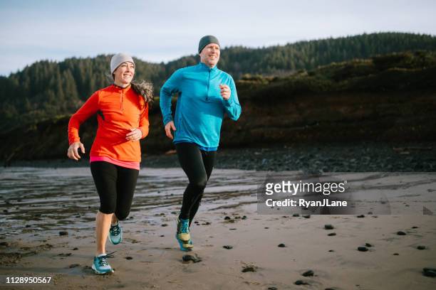 mature adult couple jogging on the beach - mature couple winter outdoors stock pictures, royalty-free photos & images
