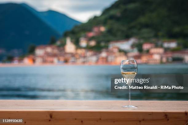 glass of franciacorta wine with the view of monte isola, during the installation "the floating piers" by christo on iseo lake. - iseo lake stock pictures, royalty-free photos & images