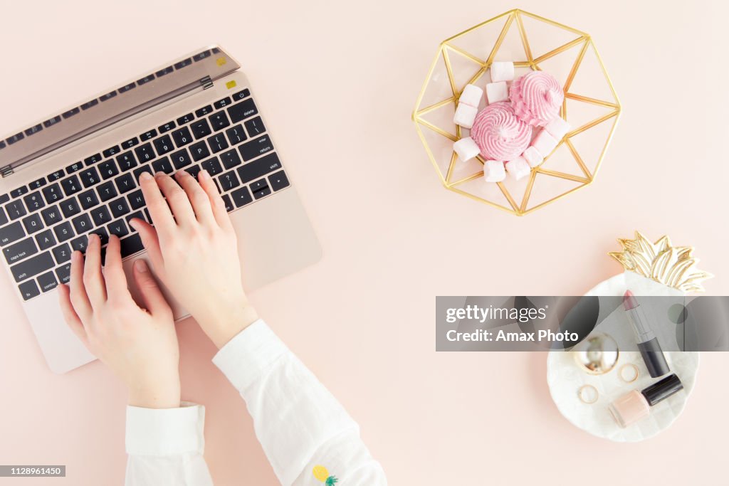 Workspace with laptop, woman hands on pastel pink background. Flat lay, top view office table desk.