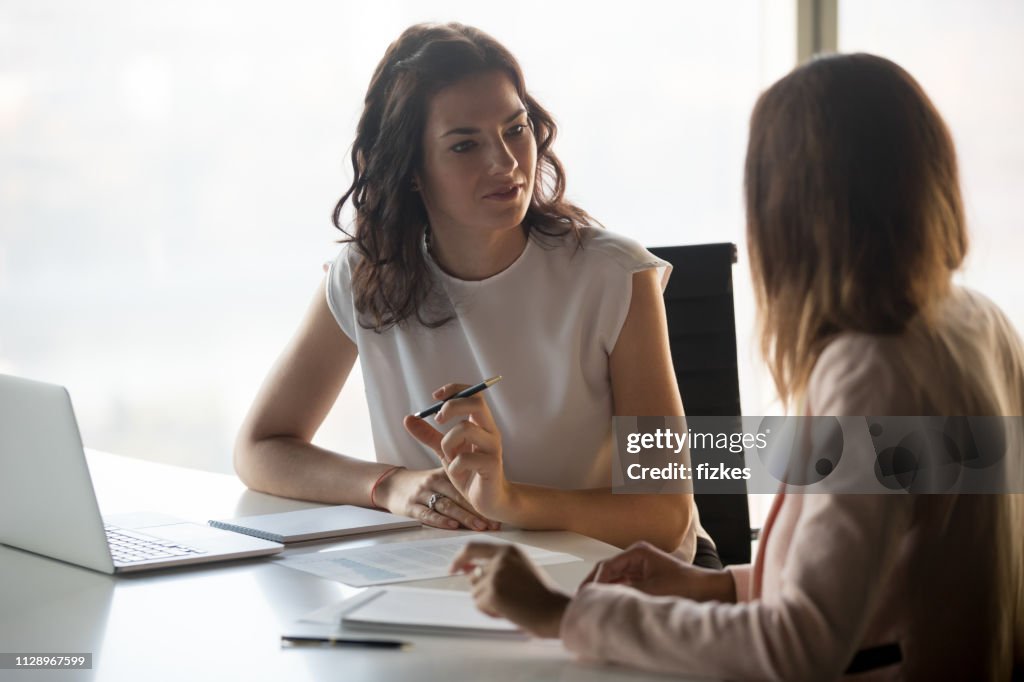 Two diverse serious businesswomen talking working together in office