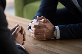 Clasped male hands of two businessmen negotiating at table