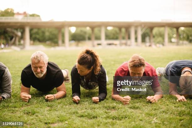 determined male and female friends doing plank exercise together in park - krafttraining stock-fotos und bilder