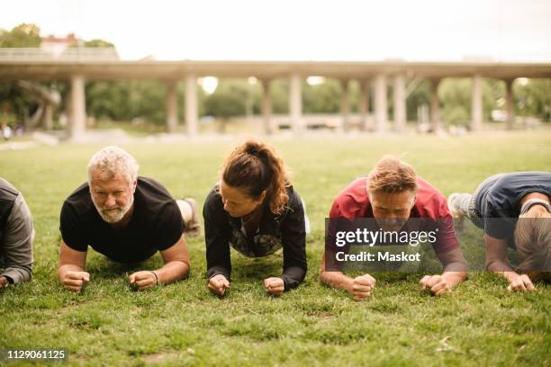 determined male and female friends doing plank exercise together in park - postura de plancha fotografías e imágenes de stock