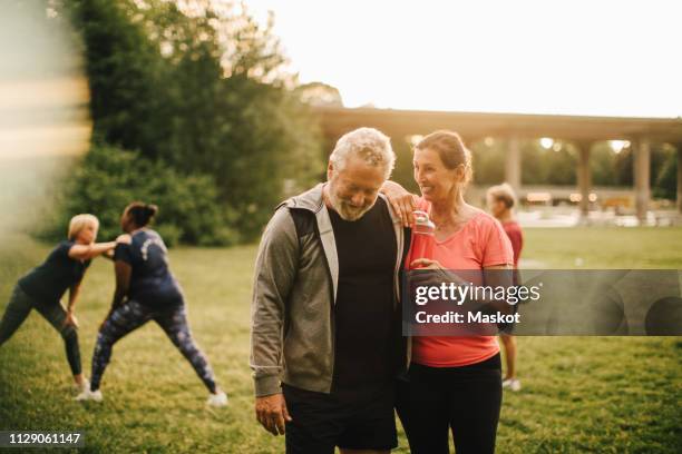 smiling active male and female talking while friends exercising in background at park - african man white background stock pictures, royalty-free photos & images