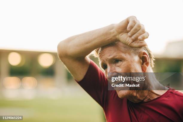 senior man rubbing face while sweating during workout at park - sweat fotografías e imágenes de stock