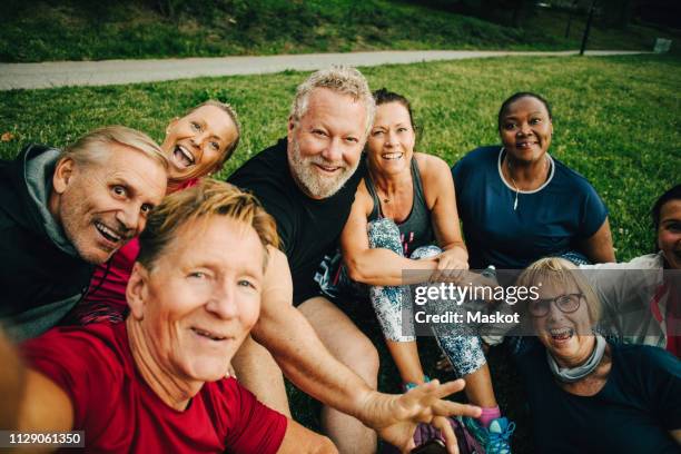 high angle portrait of happy friends taking selfie while sitting on field at park - adults working out foto e immagini stock