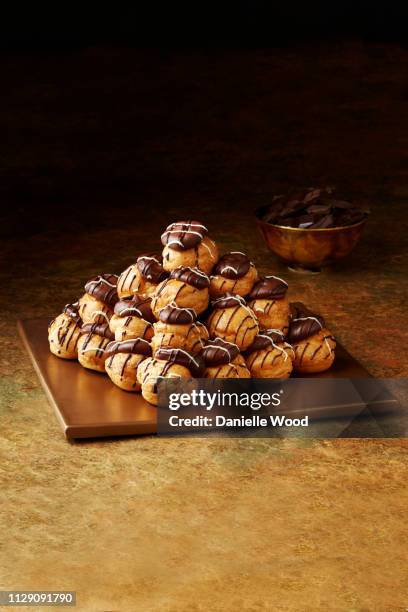 still life with stacked chocolate profiteroles on gold plate, christmas dessert - profiterole stock pictures, royalty-free photos & images