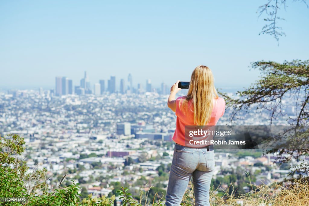 Young woman photographing skyline from hilltop, rear view, Los Angeles, California, USA