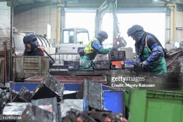 Workers in protective clothing cutting up automotive batteries in vehicle battery recycling plant