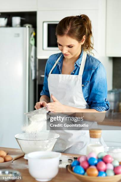 woman sifting flour into mixing bowl in kitchen - sifting stockfoto's en -beelden