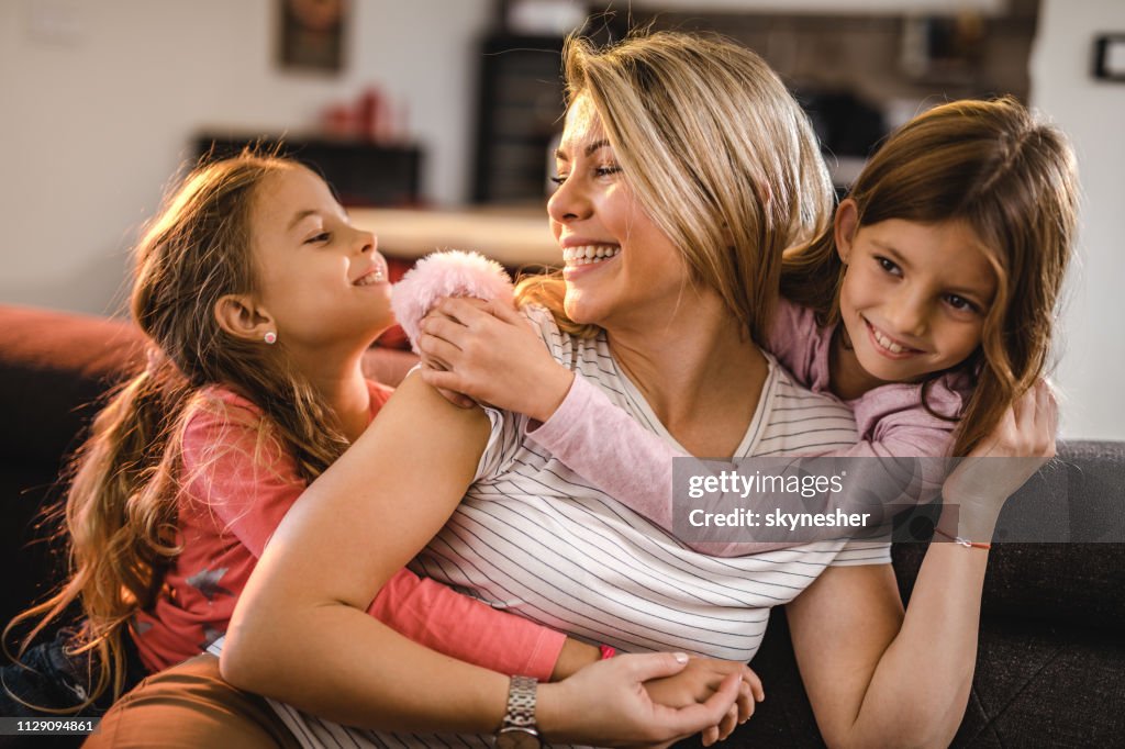 Lycklig mamma njuter i en kram av hennes två små döttrar hemma.