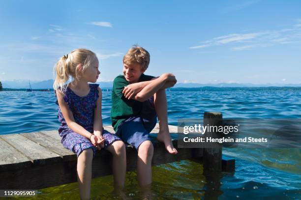 siblings cooling feet in water, lake starnberg, bavaria, germany - bavaria girl stockfoto's en -beelden