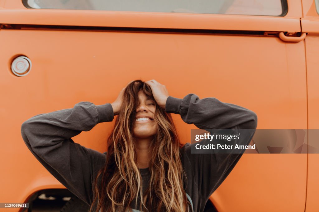 Young woman in front of orange recreational vehicle at beach, portrait, Jalama, California, USA