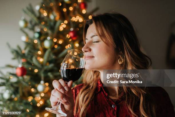 woman smelling glass of wine beside decorated christmas tree - christmas drinks stockfoto's en -beelden