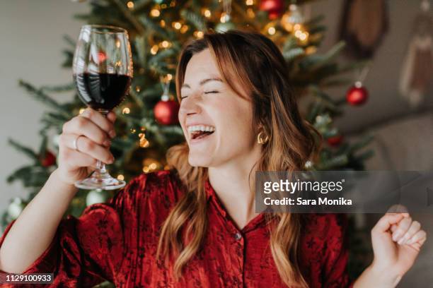woman dancing with wine beside decorated christmas tree - adult laughing christmas stock pictures, royalty-free photos & images