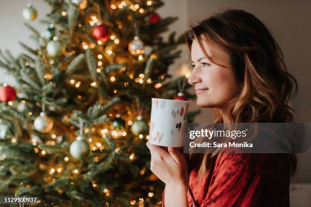 woman drinking coffee beside decorated christmas tree - christmas coffee stock pictures, royalty-free photos & images