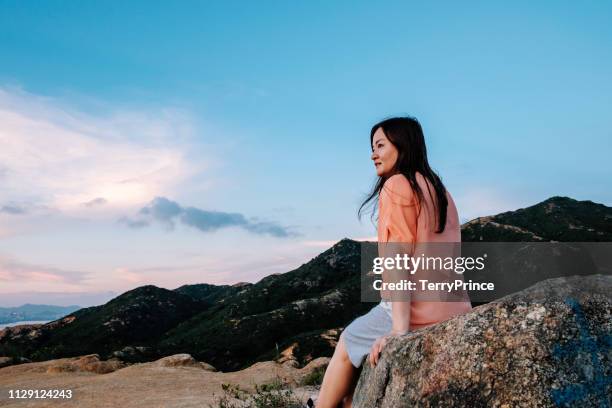 a young female is sitting on a rock enjoying this tranquil scene - tuen mun stock pictures, royalty-free photos & images